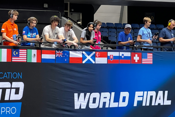 Image of the participants on the side lines wearing headset and holding remote controls for their hydrogen vehicles