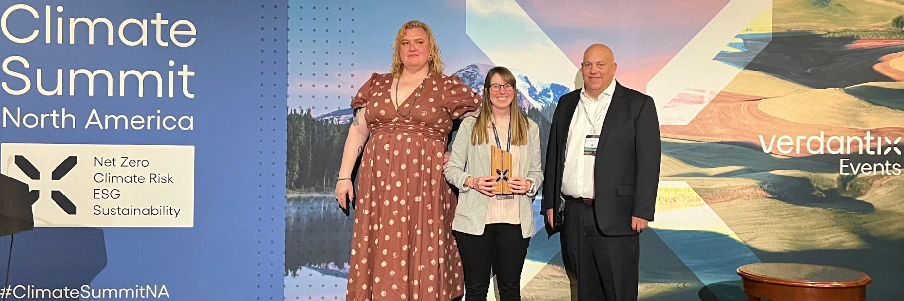 three people standing on a stage holding an award