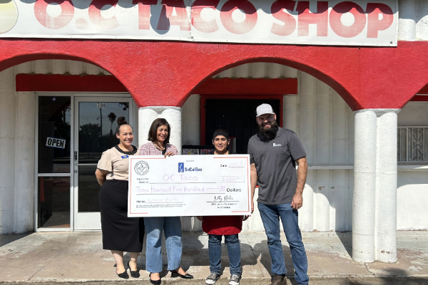 Restaurant owners posing with a giant check in front of their building