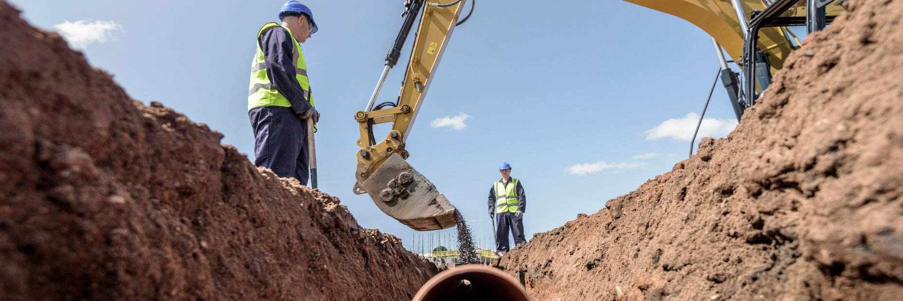 Two men working on laying and burying a pipeline in a hole