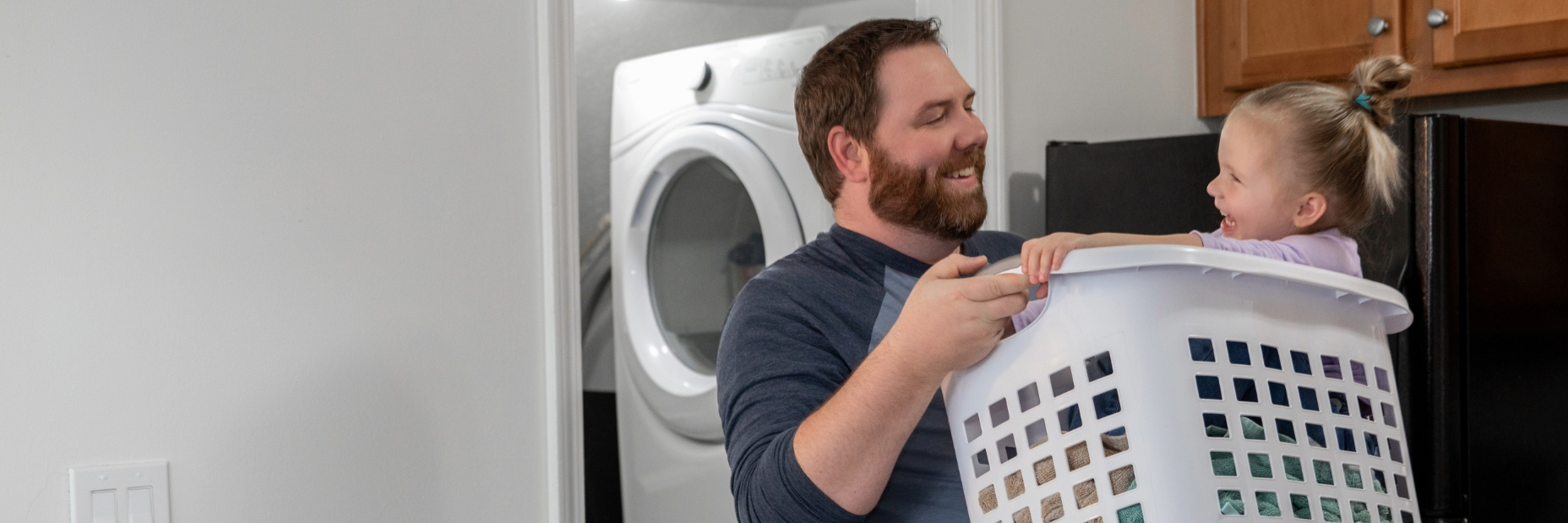 Guy laughing with his daughter who is in a laundry basket