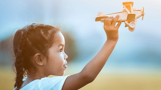 Outdoor photo of a young girl holding a wooden airplane