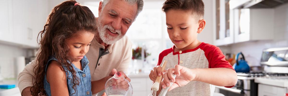 Grandfather cooking with two grandchildren in kitchen. 