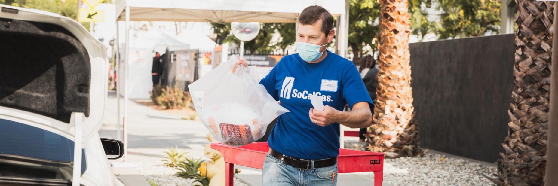 socalgas volunteer handing out thanksgiving meal supply box to vehicle