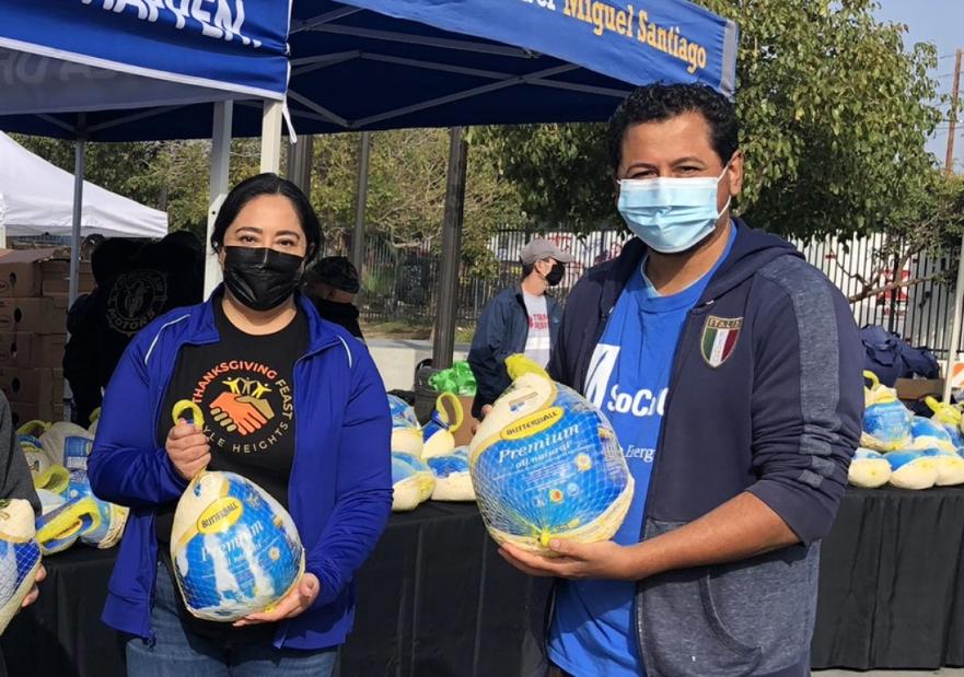 SoCalGas volunteers holding frozen turkeys with tables of frozen turkeys behind them