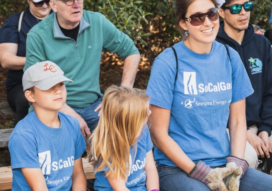 People wearing socalgas tee shirts and gloves sitting on bleachers