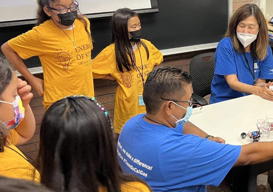 students gathered around a table with two teachers