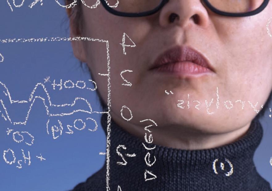 A woman writing symbols and equations on a glass board with white chalk.