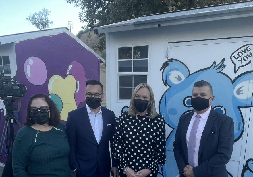 People posing for image in front of tiny homes at a press event