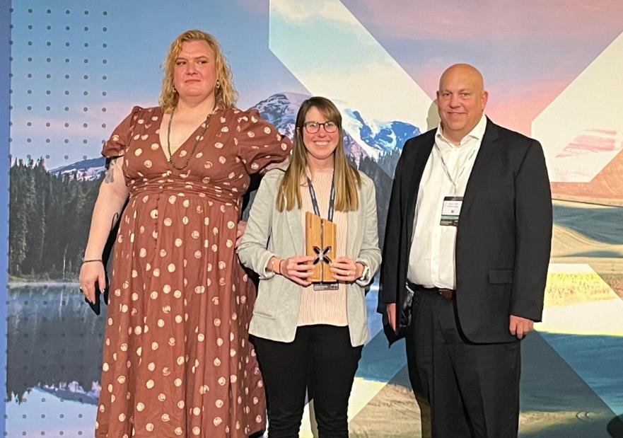 three people standing on a stage holding an award