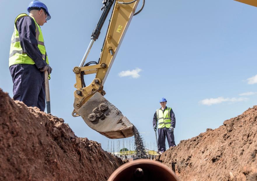 Two men working on laying and burying a pipeline in a hole