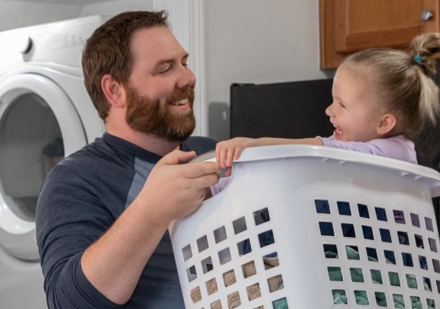 Guy laughing with his daughter who is in a laundry basket