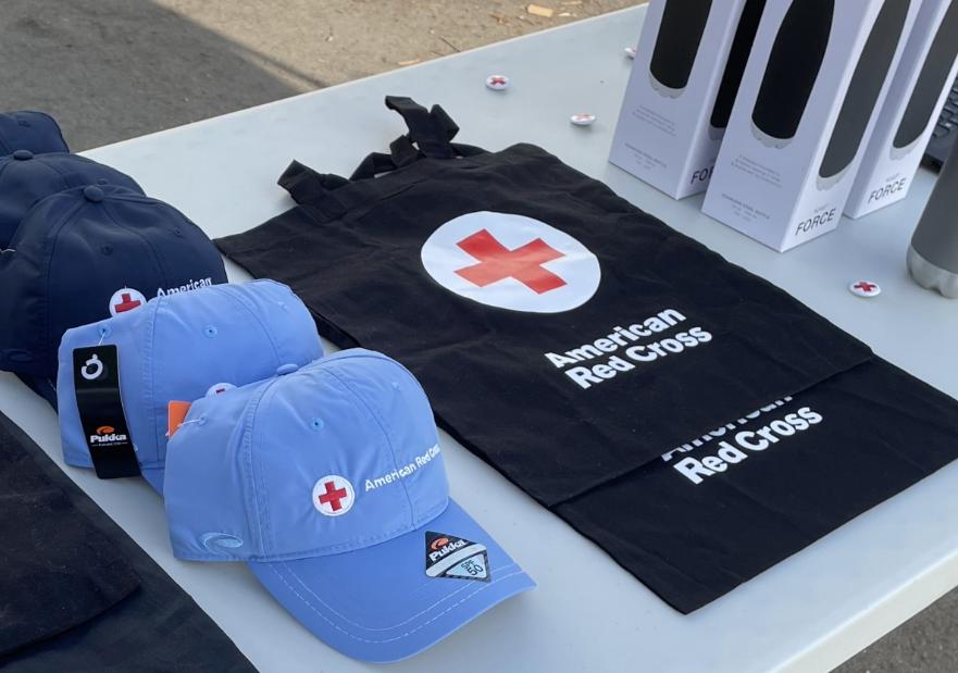 A table with american red cross hates, bags, and tumblers on it.