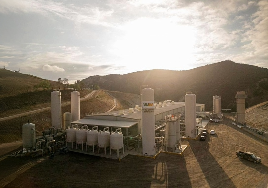 Waste management facility up against a hill with the sun starting to shine behind the hill